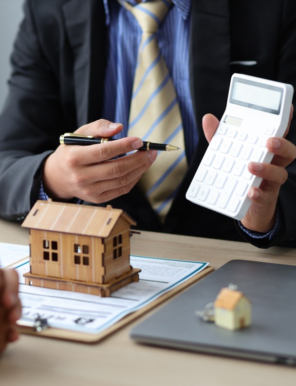 Frais de notaire – un notaire faisant une simulation des frais d’acquisition avec une calculatrice et une maison en bois miniature devant lui