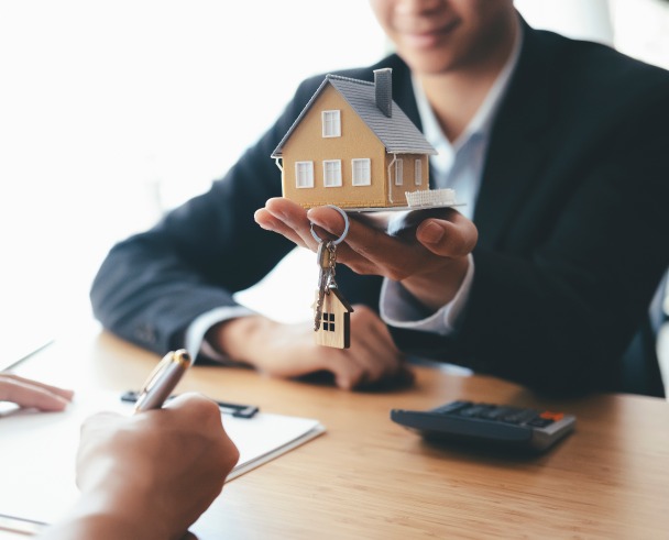 Achat immobilier – un agent immobilier tenant une miniature de maison et des clés dans sa main