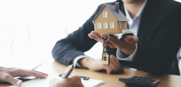 Achat immobilier – un agent immobilier tenant une maison miniature et des clés dans sa main