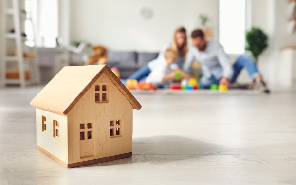 Assurance habitation – une maison en bois miniature devant une famille jouant avec son enfant