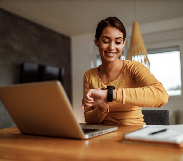 Compromis de vente – une femme souriante et regardant sa montre devant son ordinateur